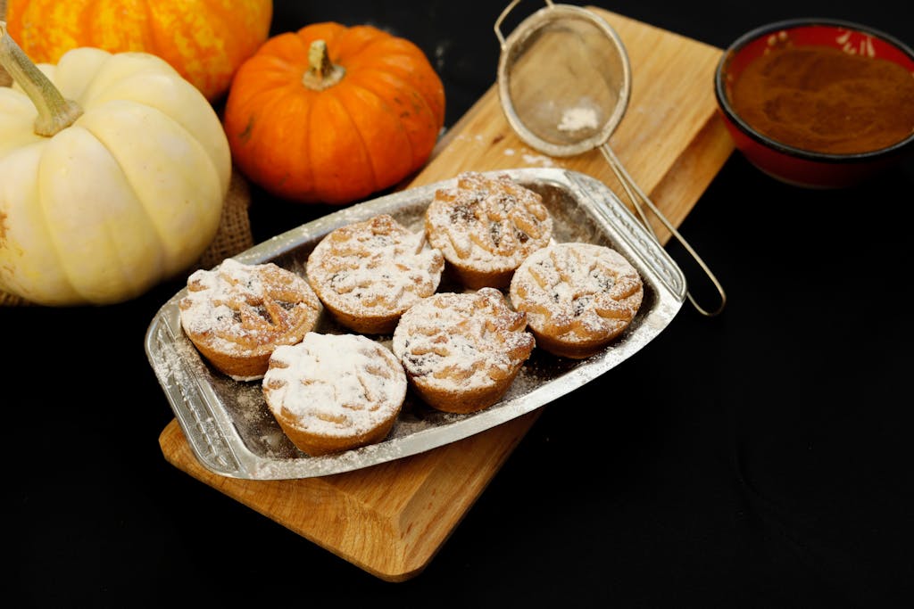 Tasty pumpkin spice muffins dusted with sugar, surrounded by pumpkins and spices, perfect for autumn treats.